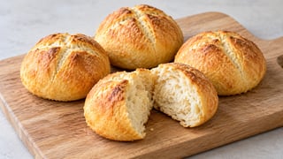 Cuatro pequeños rollos de quark marrón dorado, uno roto con migajas finas porosas