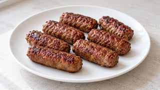 Ocho panecillos de carne de vacuno alargados dorados en una placa ligera sin acompañamientos