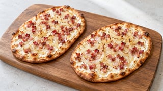 Due piccoli flammkuchen sottili con copertura cremosa, cubetti di pancetta e strisce di cipolla fini