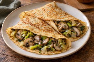 Crepes finas doradas de espelta con láminas de champiñón, puerro claro y perejil visibles