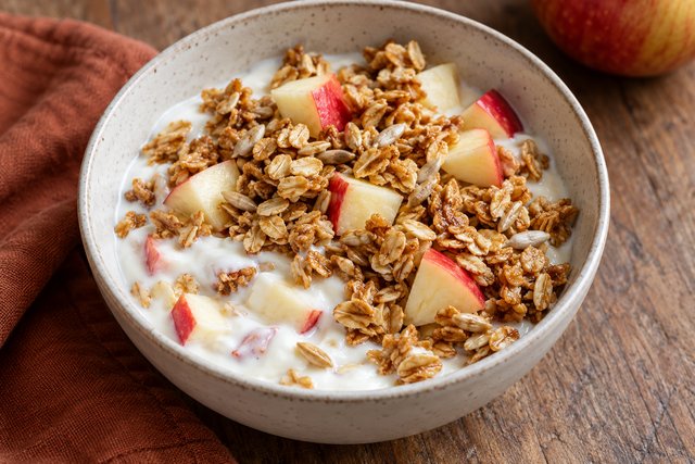 Golden oat flakes and sunflower seeds over white plain yogurt with fresh red-skinned apple cubes