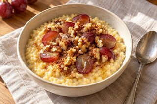 Cremiger Hirsebrei mit halbierten roten Trauben, gerösteten Walnüssen und Honig in einer Frühstücksschale