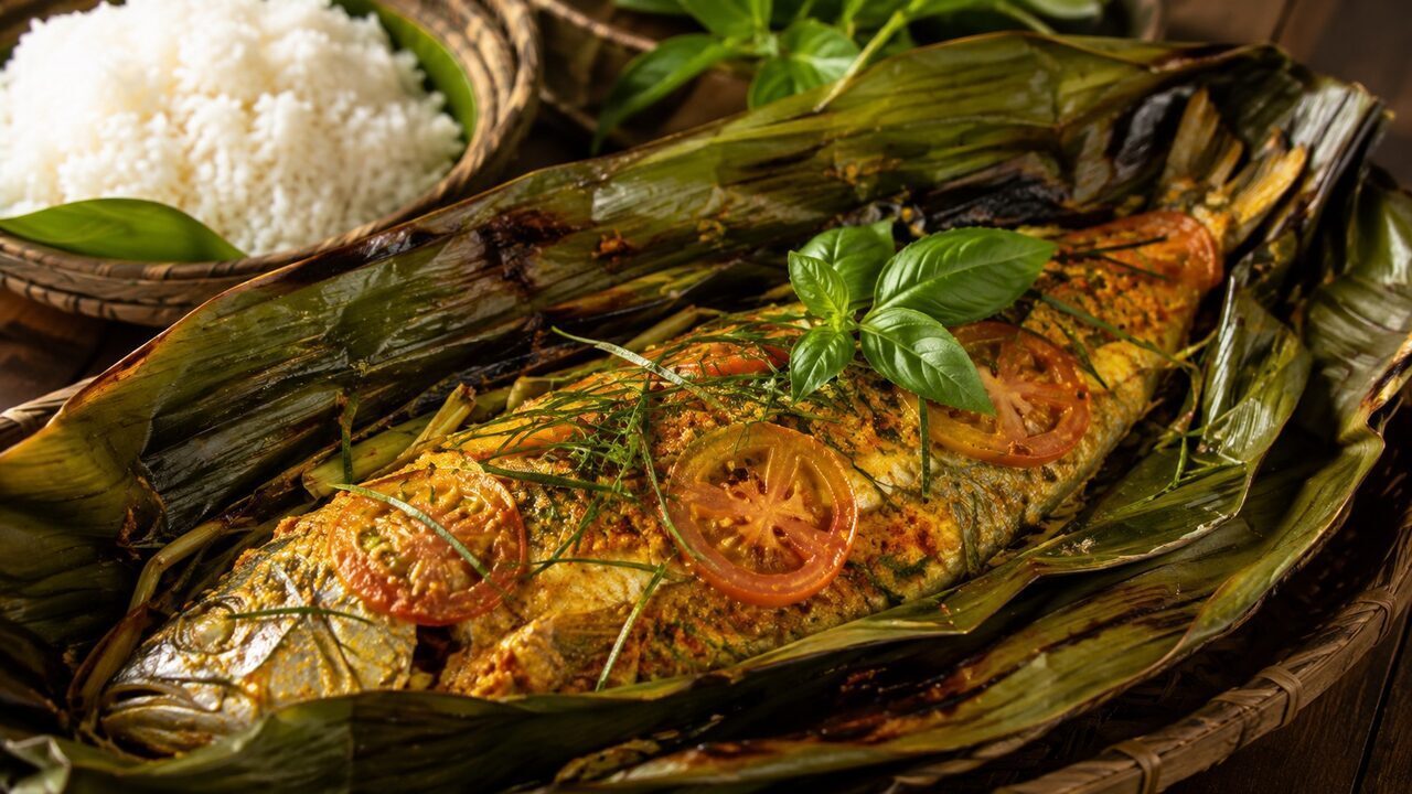 Geöffnetes Bananenblatt mit indonesischem Pepes Ikan, Makrele, Gewürzpaste, Tomaten und Basilikum